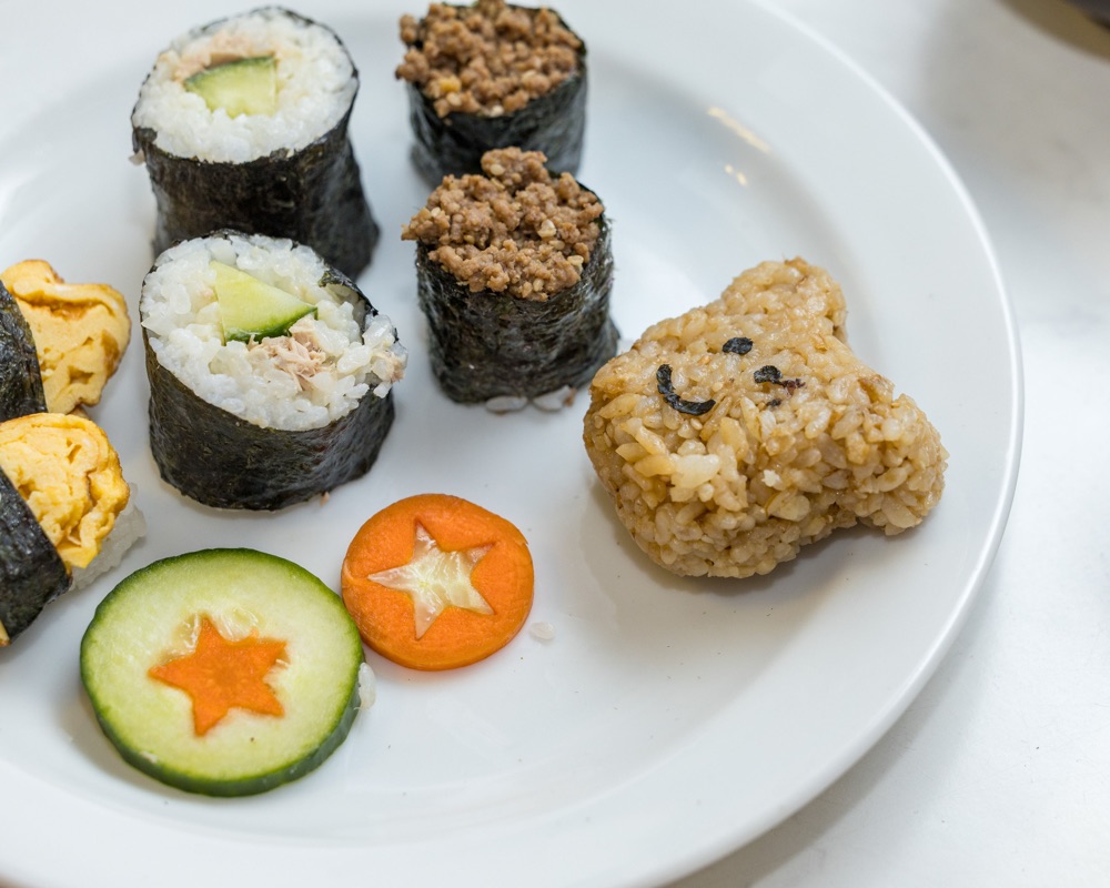 Plate of fresh maki rolls with star-shaped cucumber and carrot slices and a smiling rice-ball bear